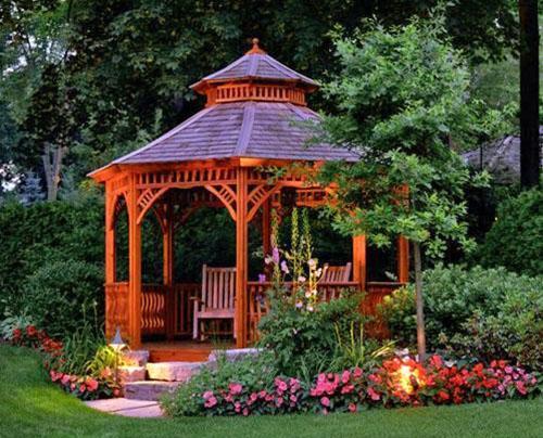 A gazebo for a summer residence made of wood with a pink flower bed
